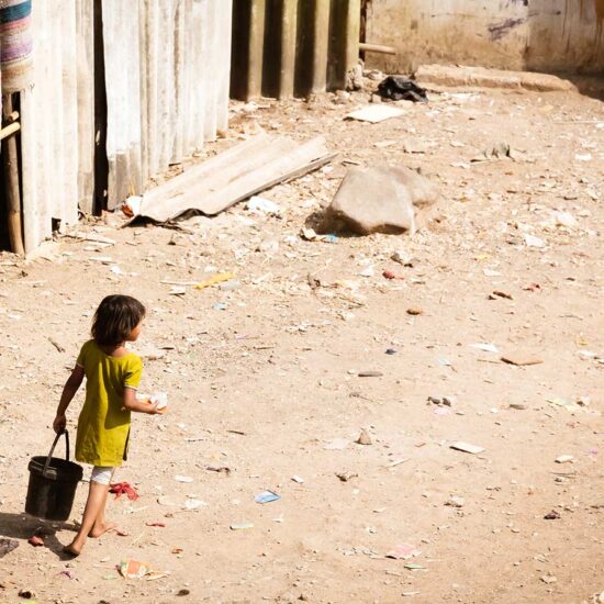 A young girl carrying a suitcase walks down the street.