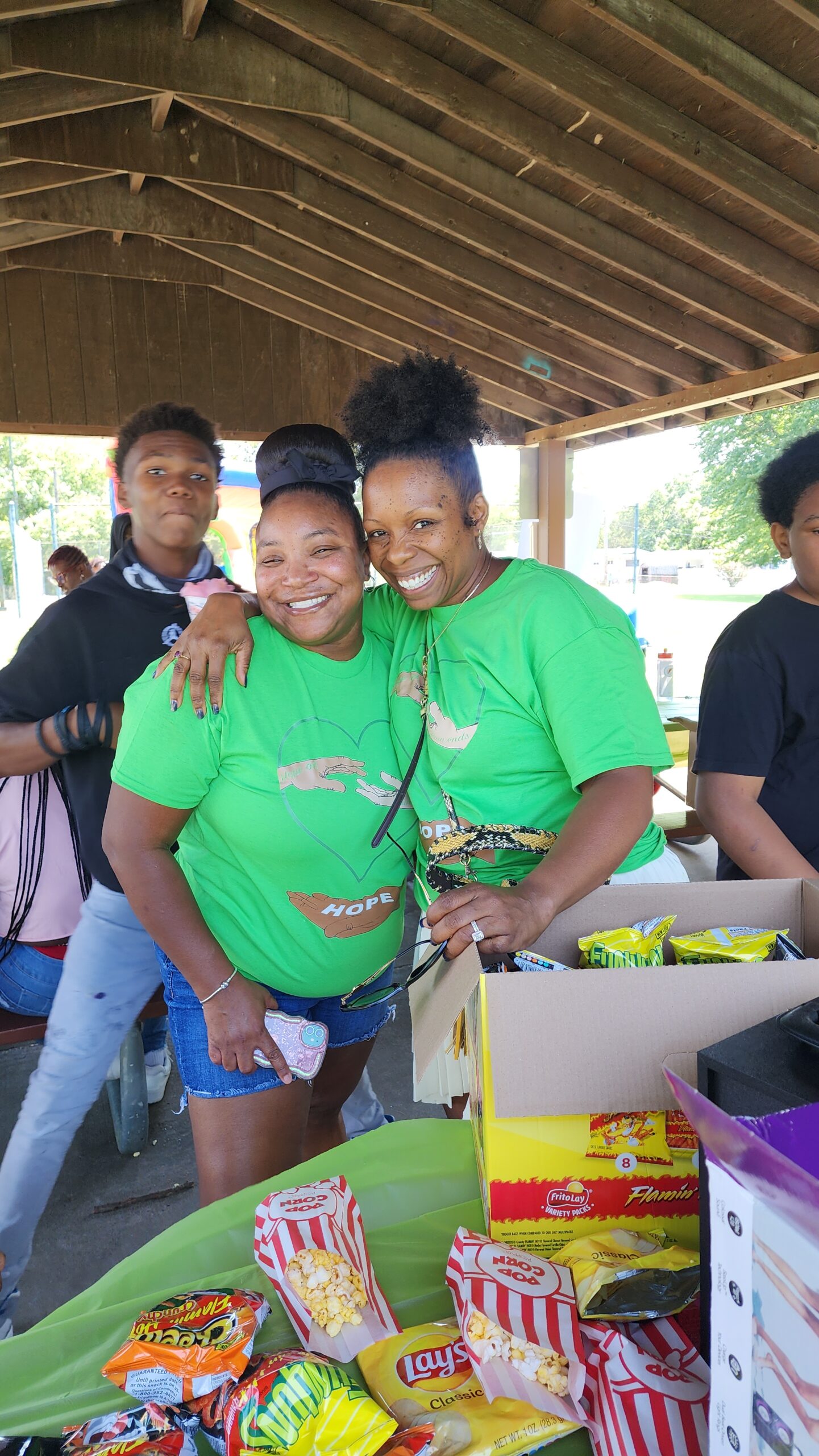 Two women in green shirts smile for a picture.